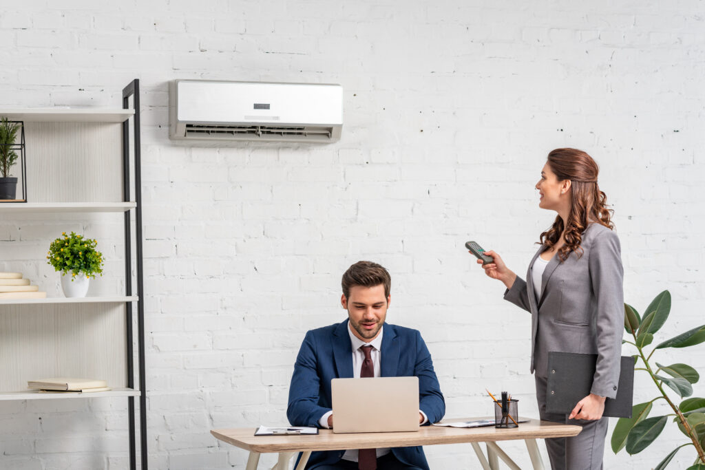 young businesswoman holding remote control while standing near man using laptop at workplace